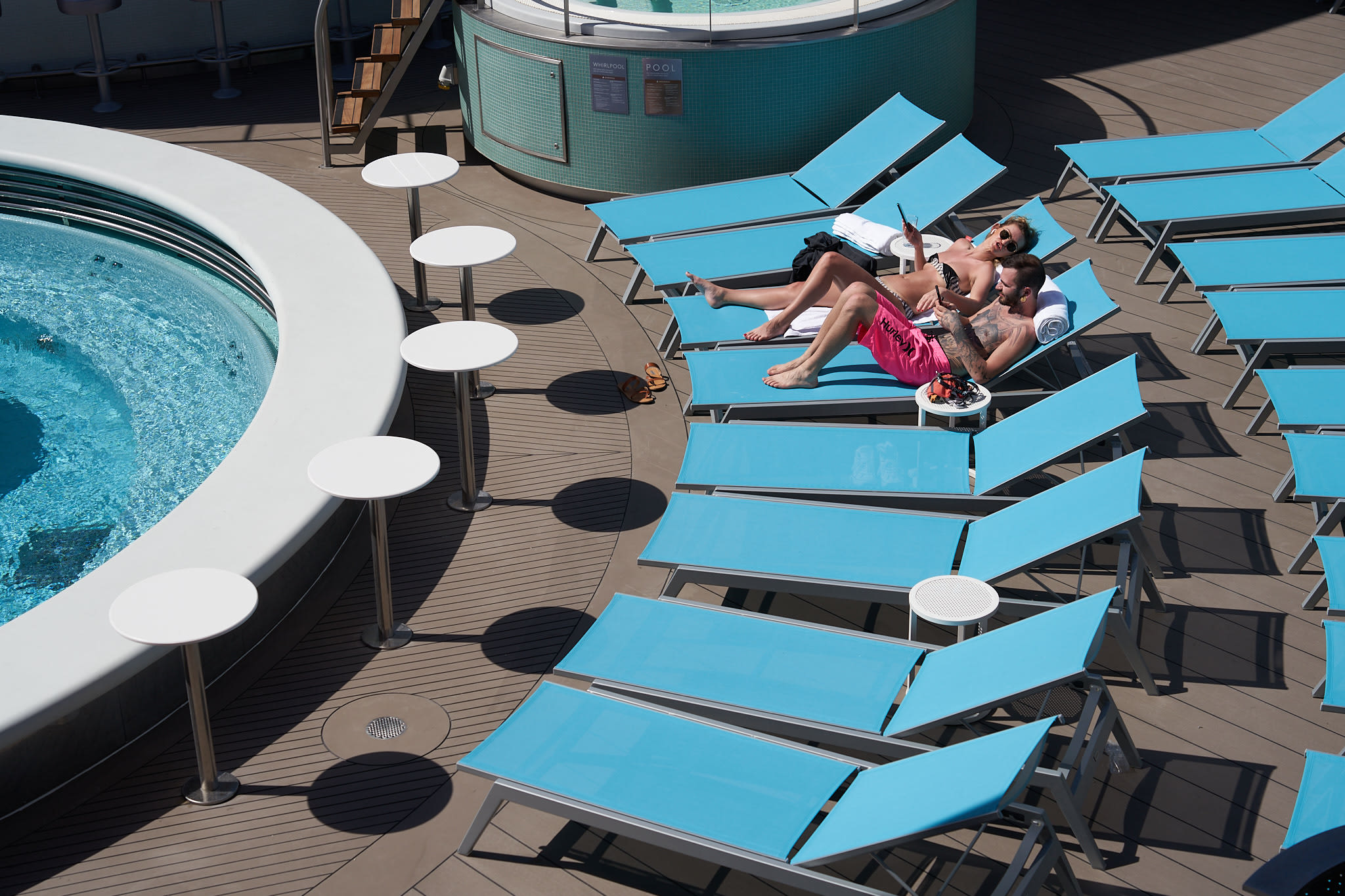 Two people laying on sun loungers by the pool on Virgin Voyages' ship Scarlet Lady