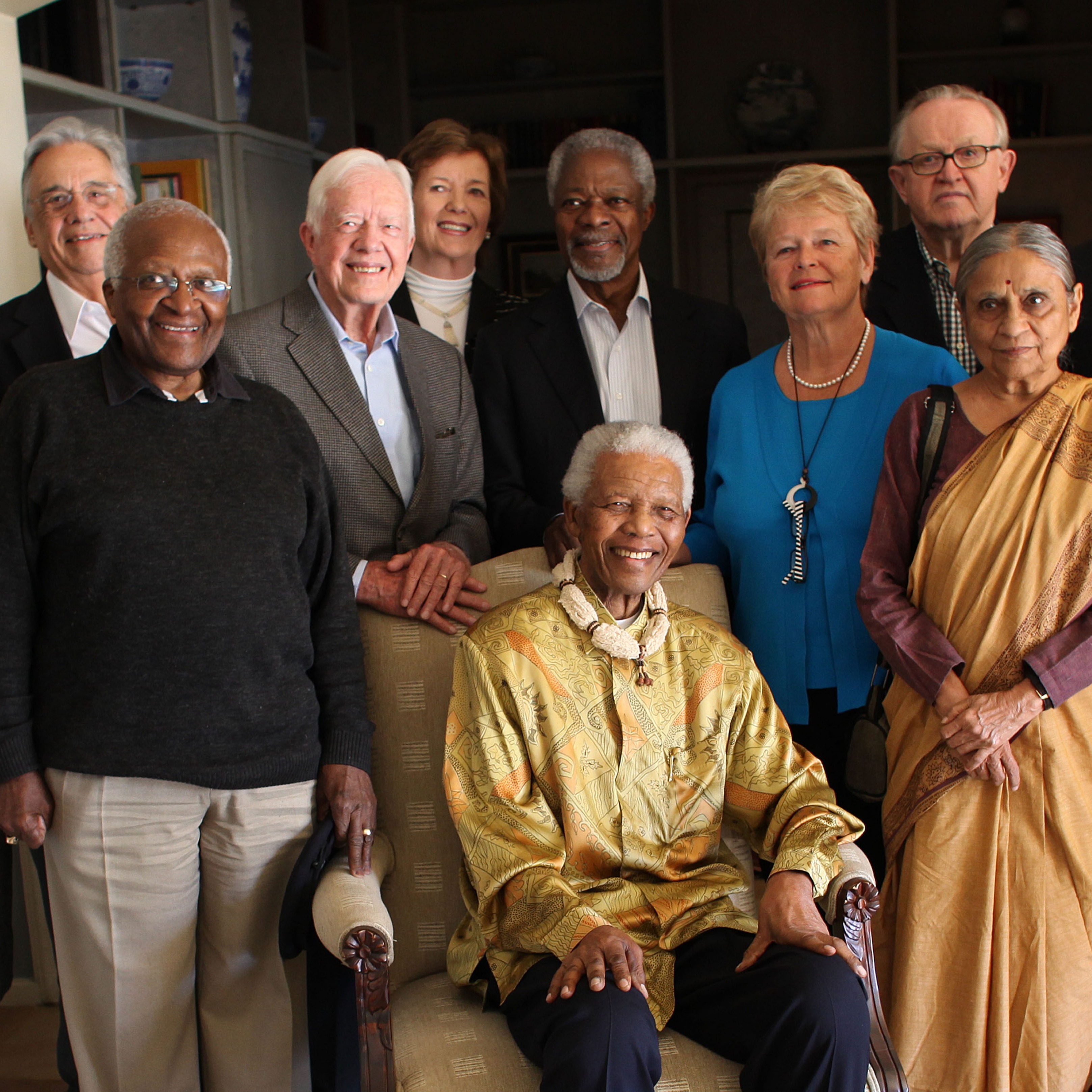 The Elders stand around a sitting Nelson Mandela