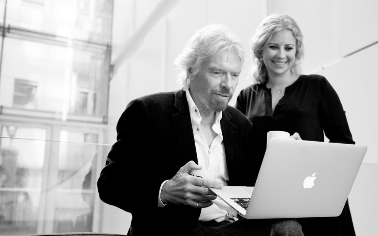 Black and White photo of Richard Branson using a laptop with Holly Branson standing next to him looking over his shoulder at the screen