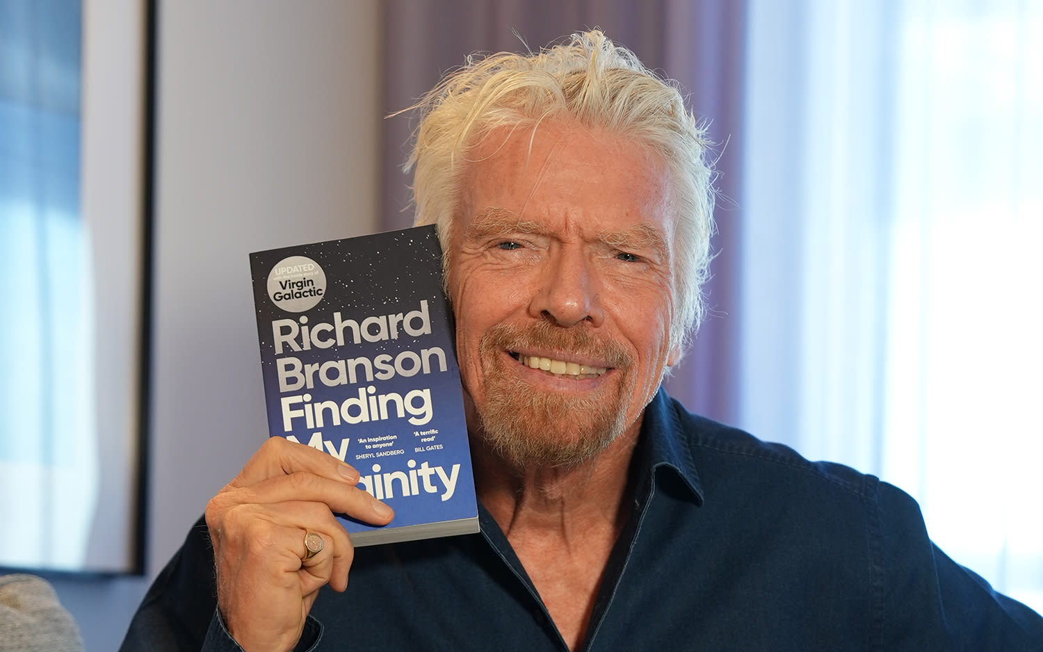 Richard Branson holding a copy of Finding My Virginity next to his face