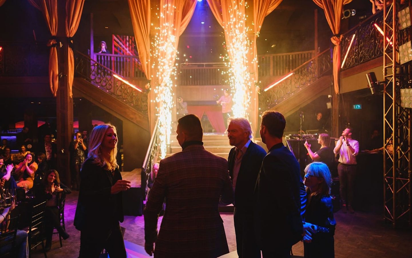 Holly Branson speaking to people at the Virgin Stars event. It is dark, with two large sparklers shooting from the floor