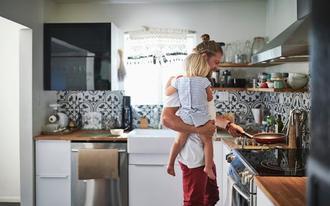 A man holding his daughter while cooking in the kitchen A man holding his daughter while cooking in the kitchen