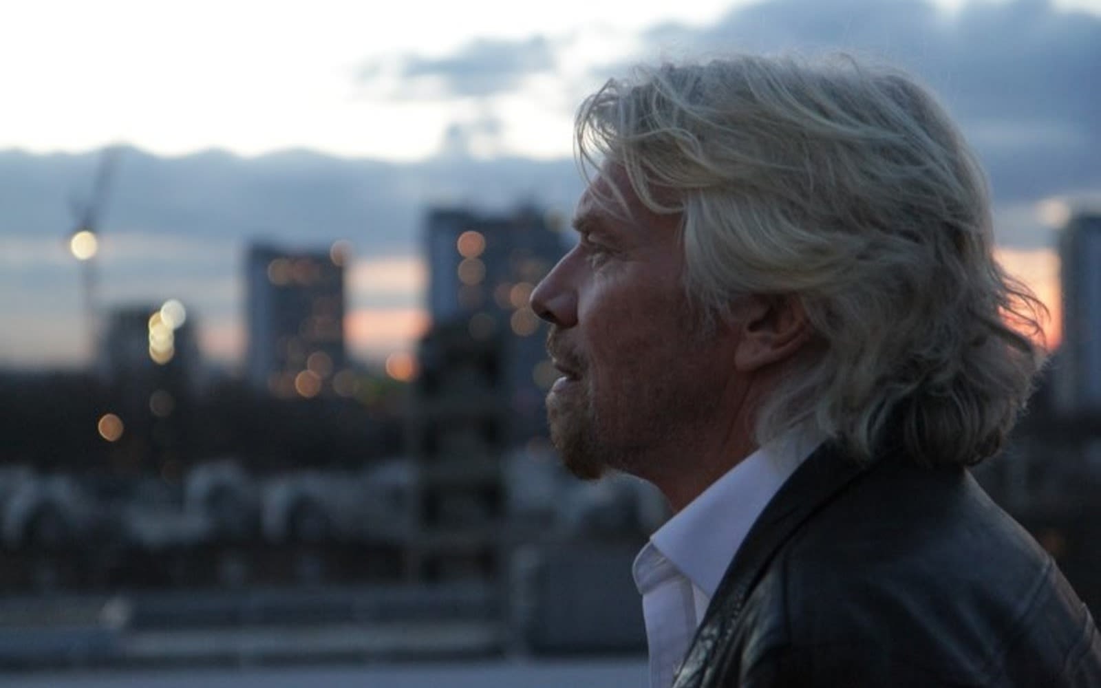 Richard Branson looking into the distance at dusk, with a city outline behind him