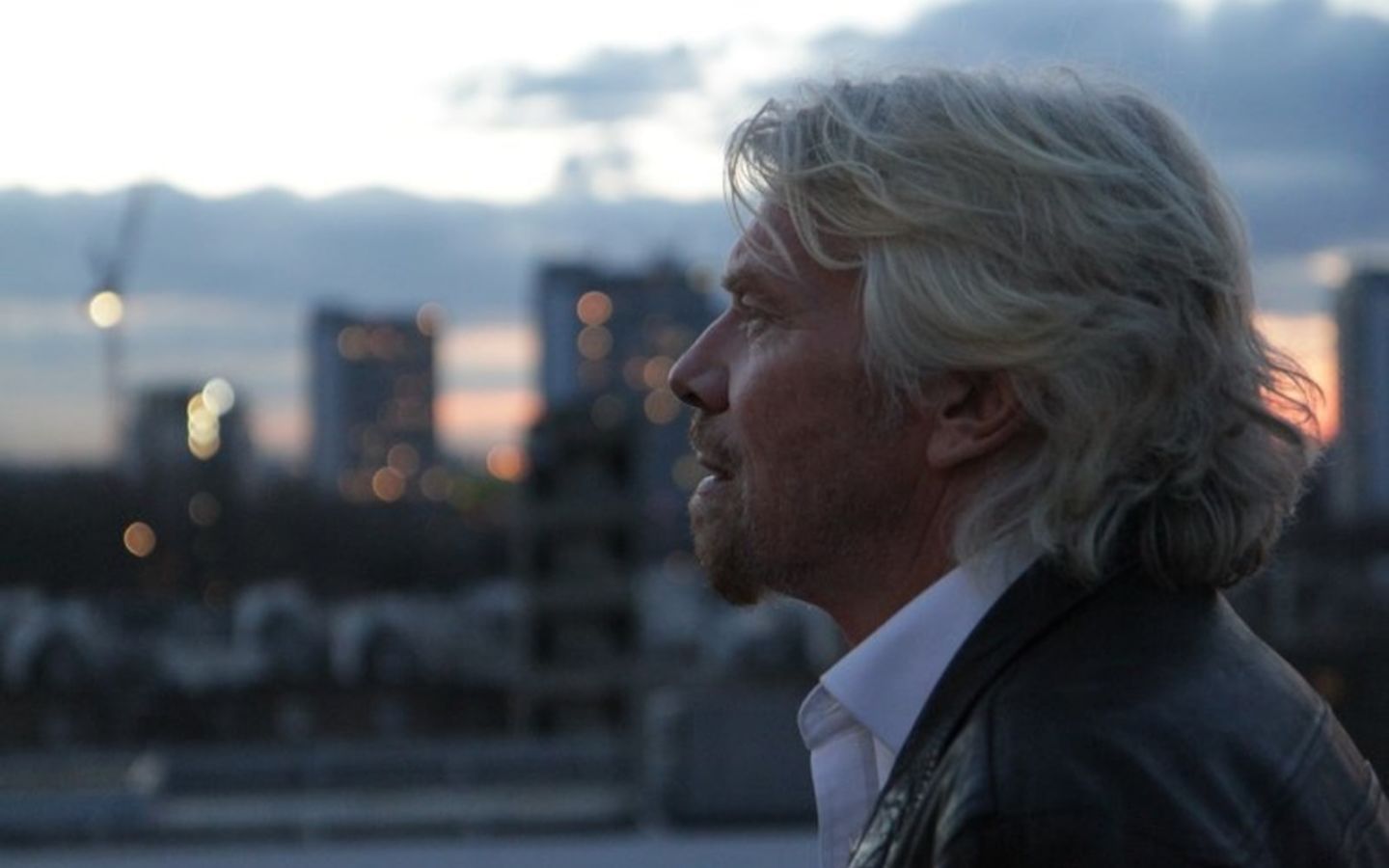 Side profile of Richard Branson looking pensive with sky and buildings in the background