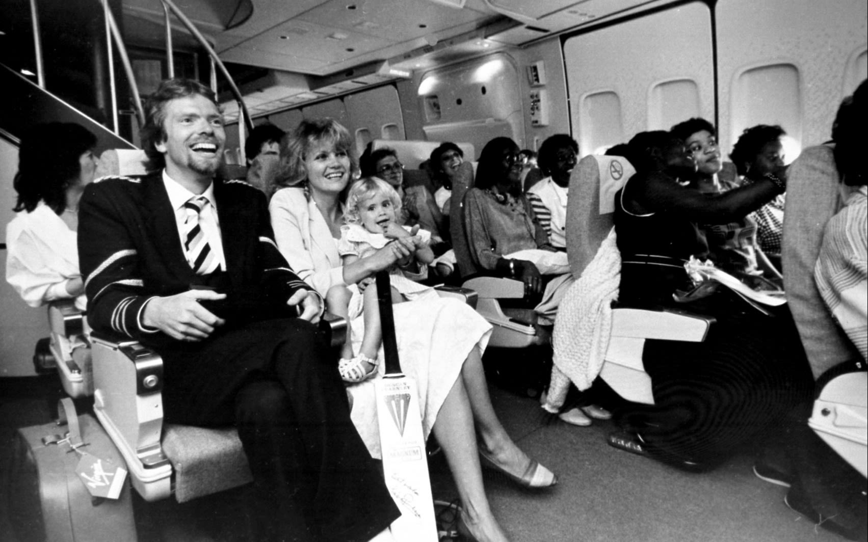 Black and white photo of Richard Branson, Joan and Holly sitting in a Virgin Atlantic plane