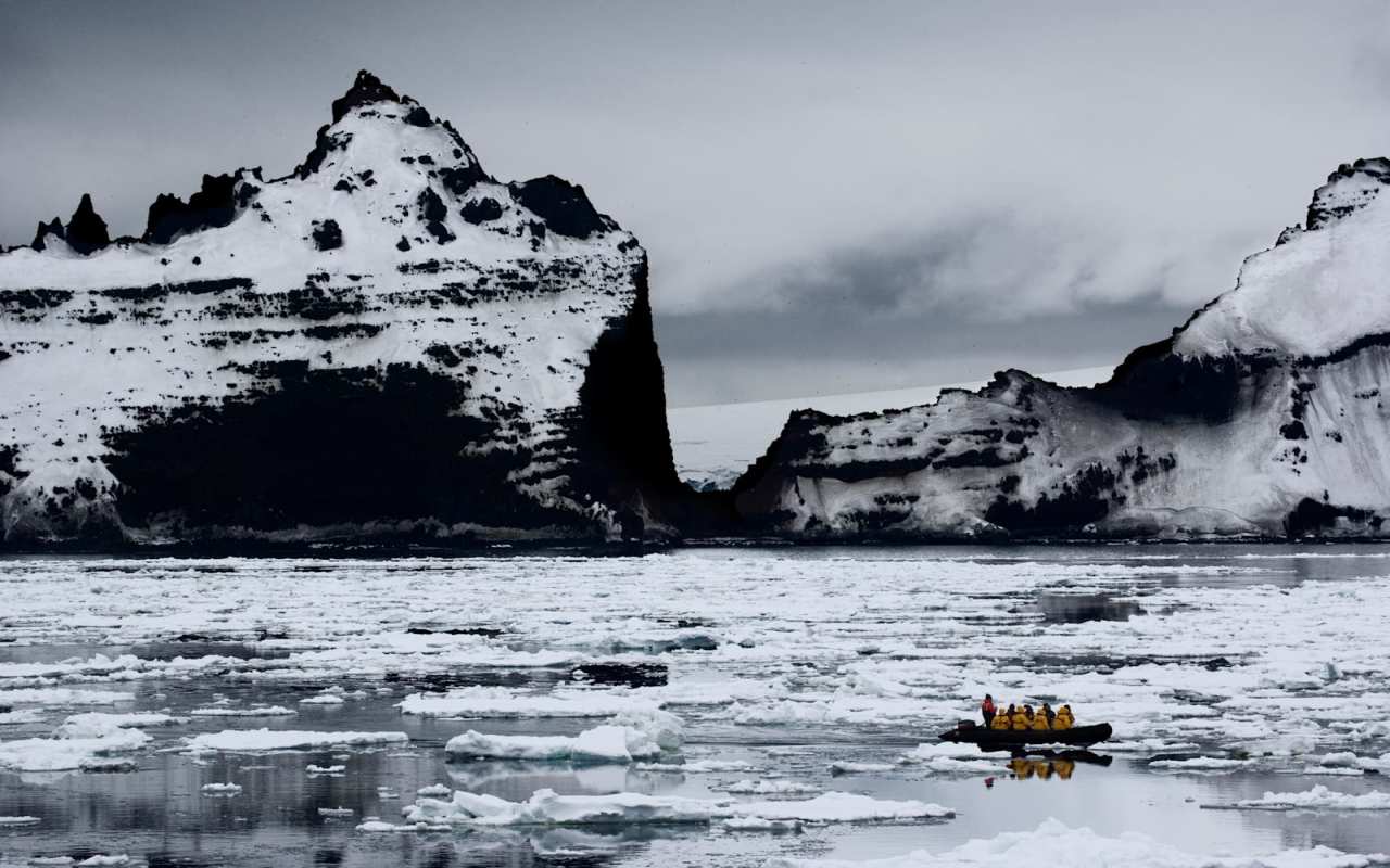 Icebergs and grey clouds are seen behind a small boat