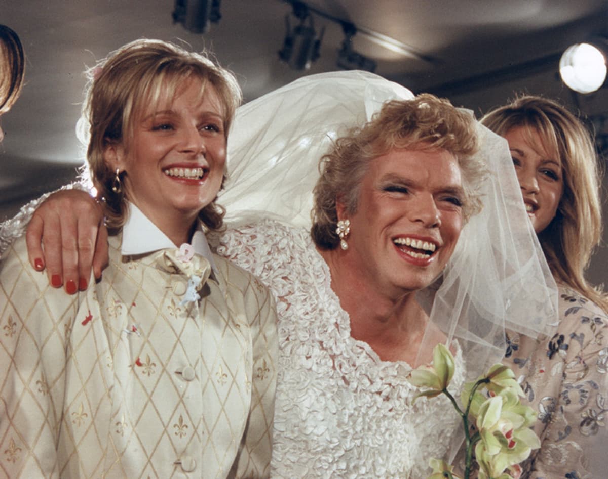 Richard Branson dressed in a veil and wedding dress, between two women, all smiling