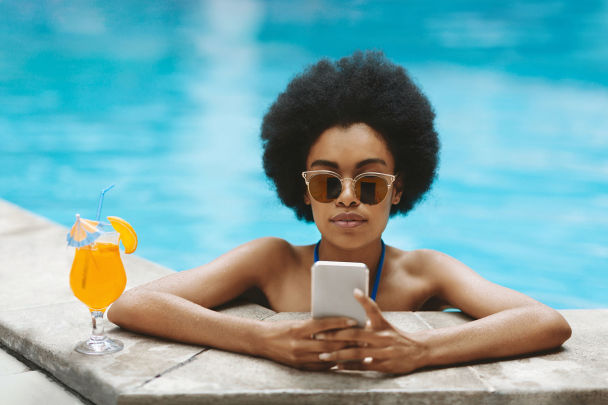 A woman using her phone in a swimming pool, with a cocktail next to her