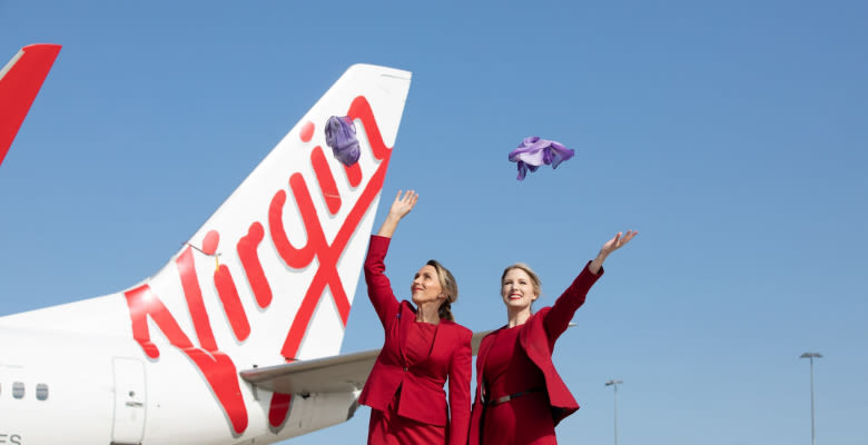 Two cabin crew members celebrate in front of a Virgin Australia plane