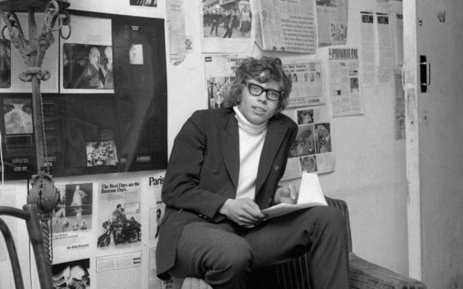 a young Richard Branson poses in front of newspaper clippings for Student Magazine