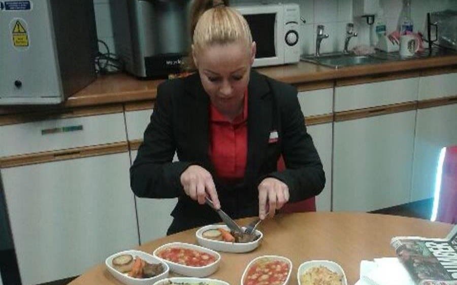 A woman in a Virgin Trains uniform sits at a kitchen table eating