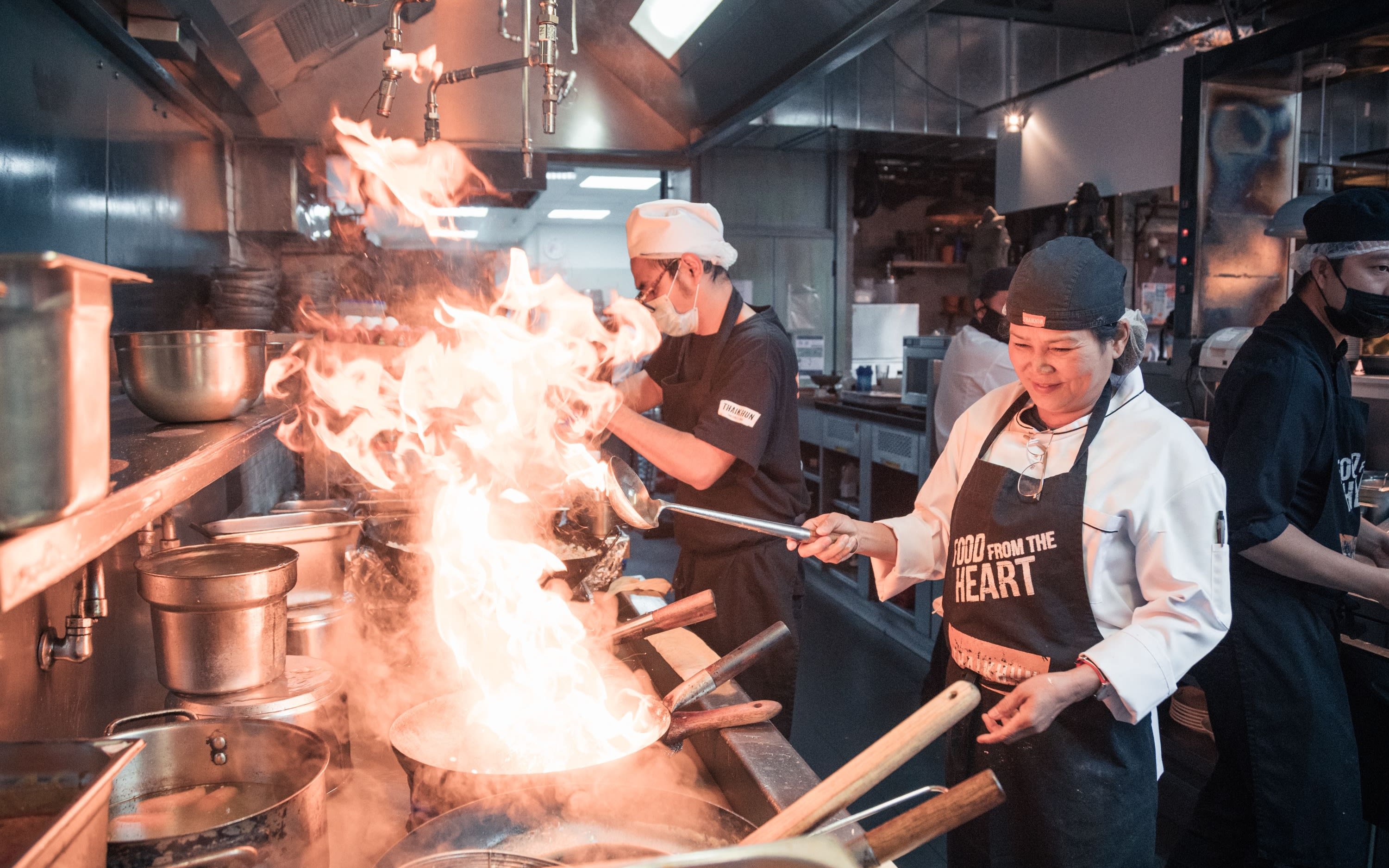 Image of a lady cooking with big flames in a Thai Masterclass in Manchester.