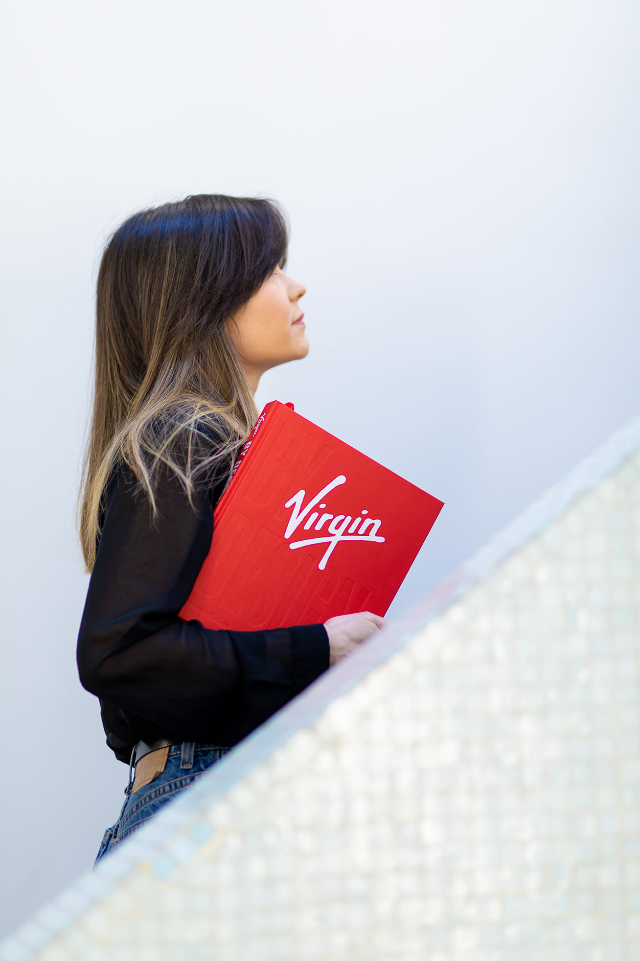 A woman walking up the stairs with a Virgin by Design book under her arm