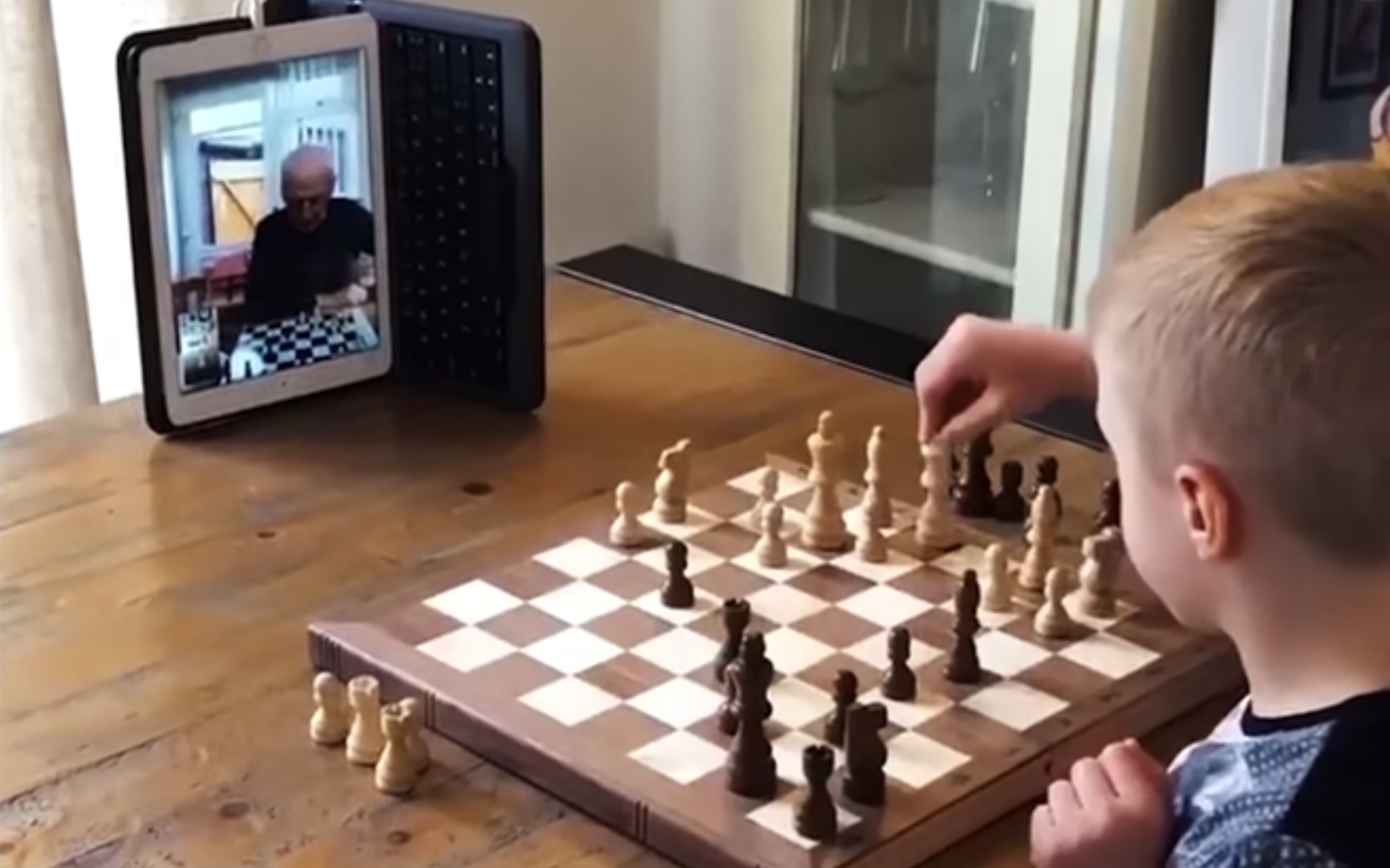 A young boy plays chess with his grandparent via video call on a tablet
