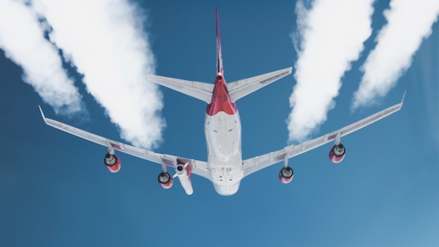 The white and red underside of Cosmic Girl Launcher One, with four jet streams trailing behind, against a blue sky
