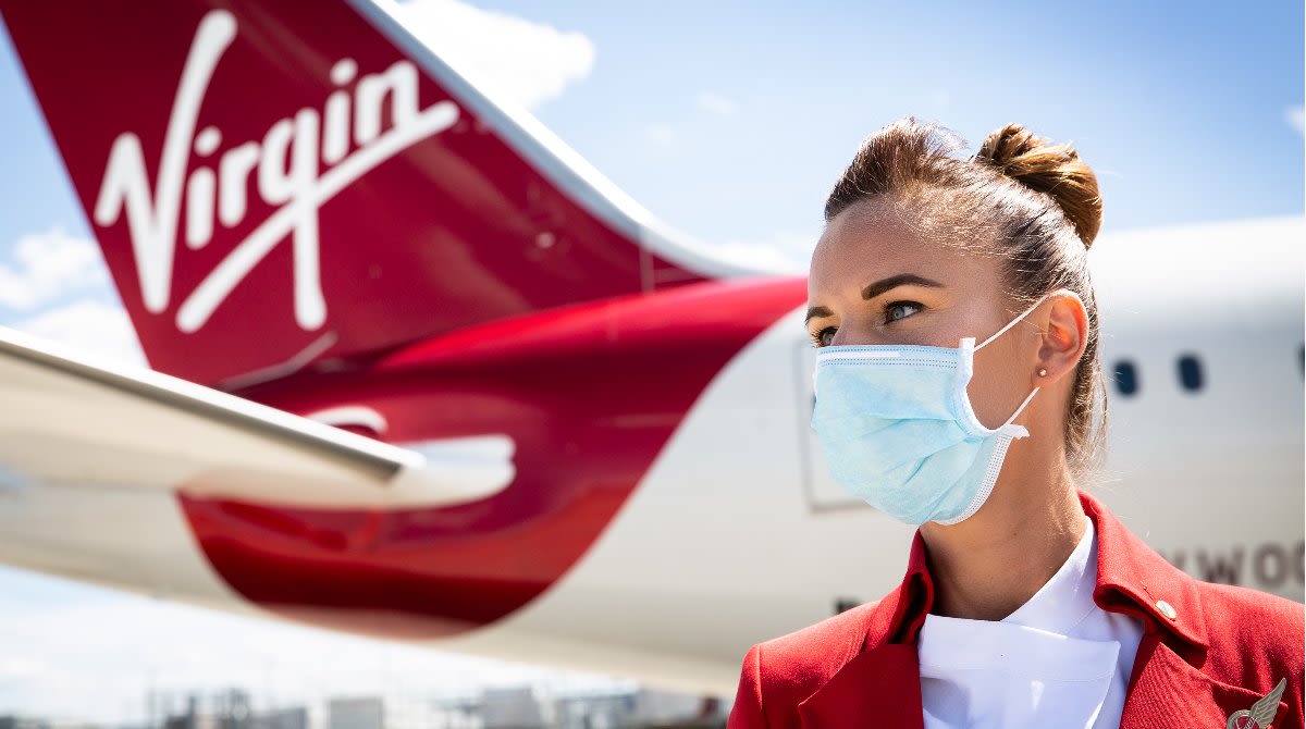 A Virgin Atlantic cabin crew member wears a face mask and stands in front of a plane