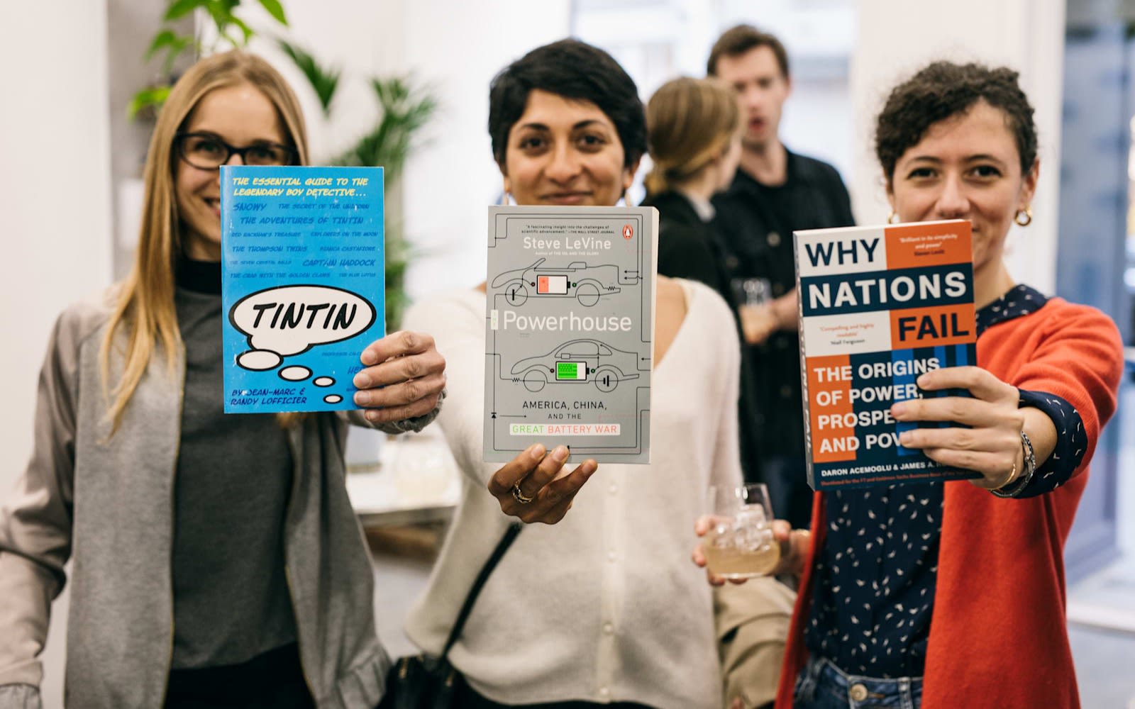 Rebel Book Club members. Three women stand shoulder to shoulder holding a book towards the camera. The book titles are TinTin, Powerhouse and Why Nations Fail