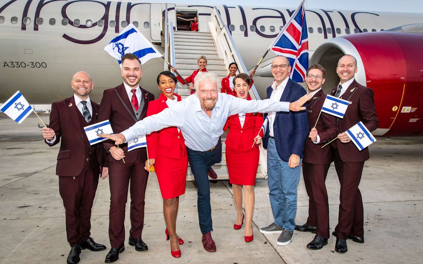 Richard Branson and cabin crew stand in front of a plane holding Union and Israeli flags