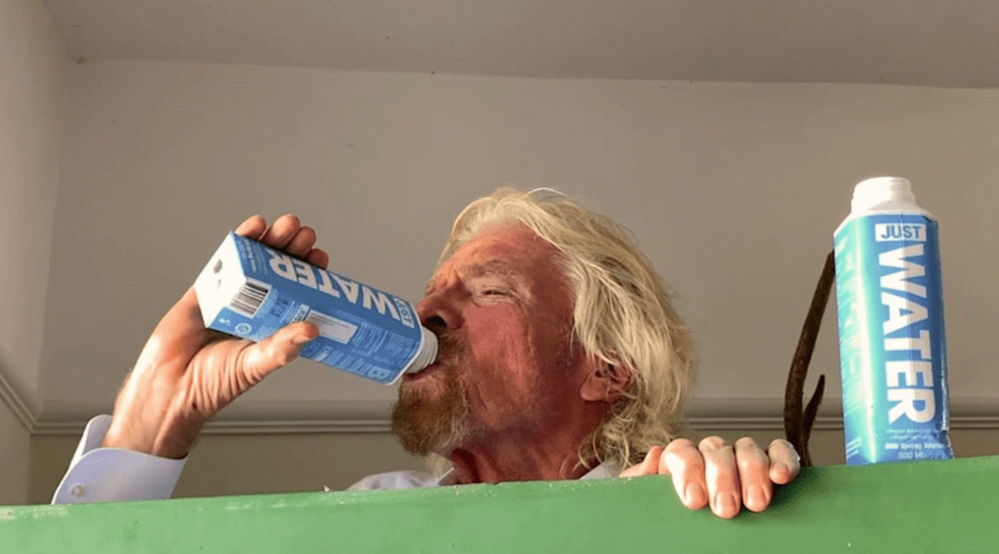 Richard Branson drinking a carton of Just Water, with another carton by his side
