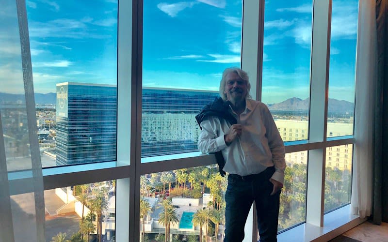 Richard Branson at the Virgin Hotel in Las Vegas standing by the window with his jumper over his left shoulder
