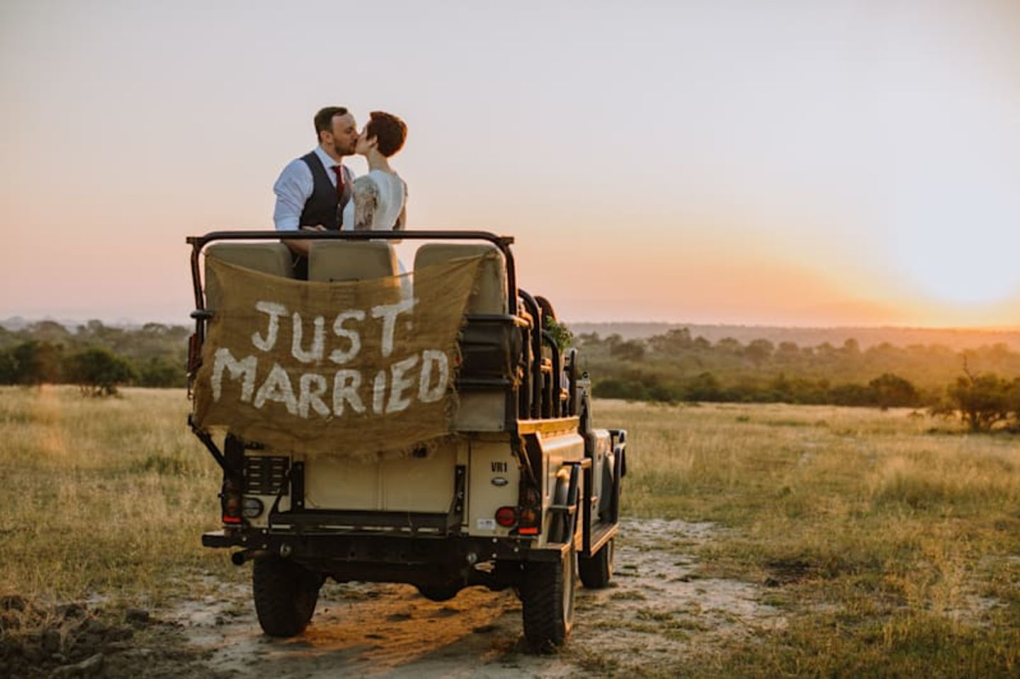 A couple kiss in a safari jeep with a Just Married sign on the back of it
