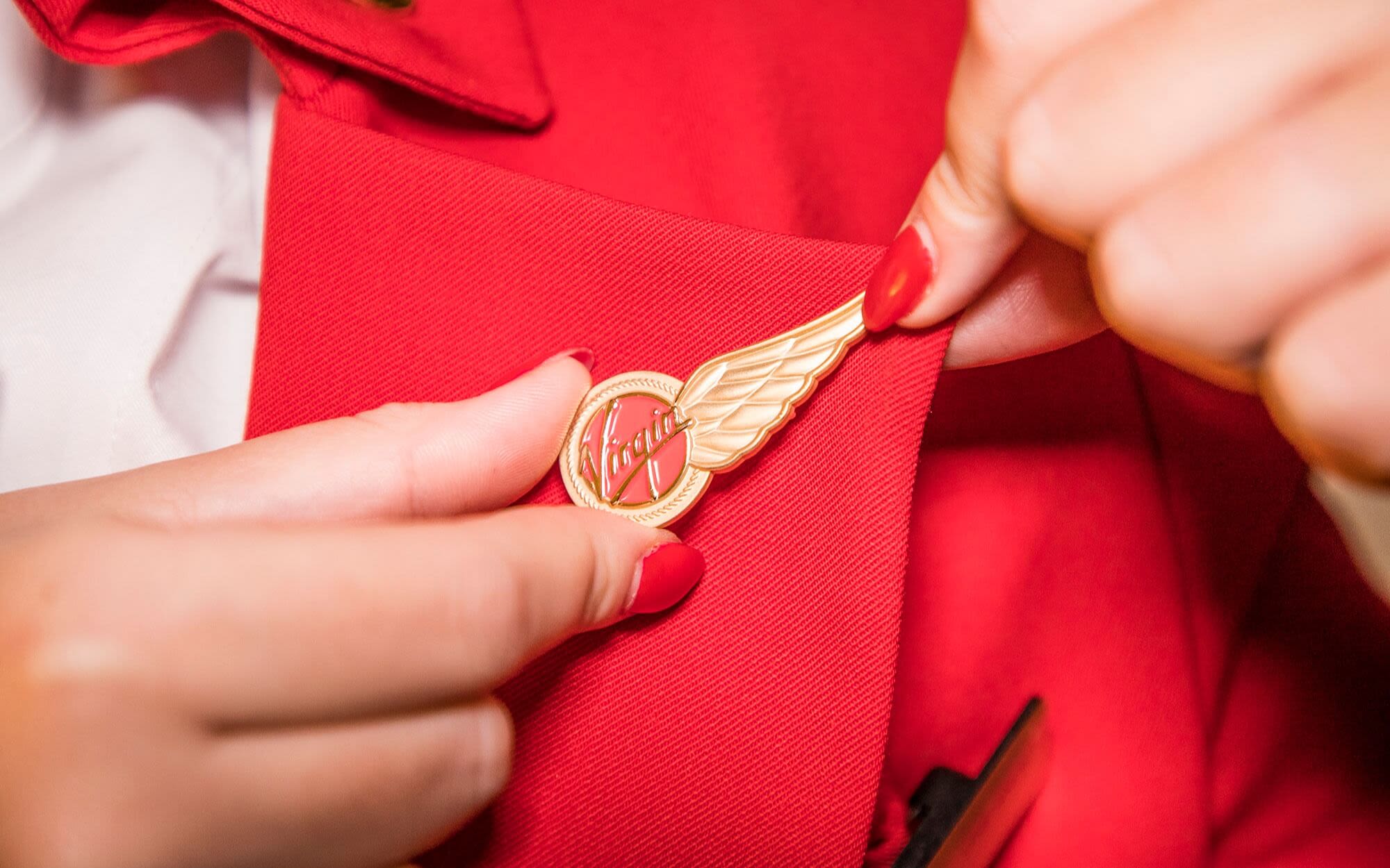 Close up of a cabin crew member in uniform and with red nail polish, adjusting their wings on their uniform