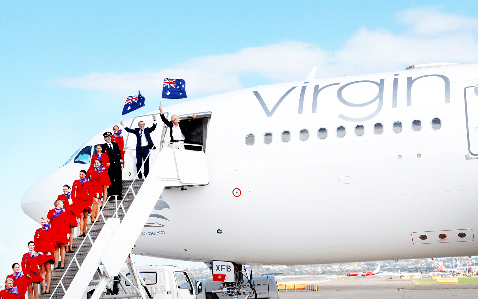 Richard Branson and Virgin Australia employees fly the Australian flag on the steps of a Virgin Australia aeroplane