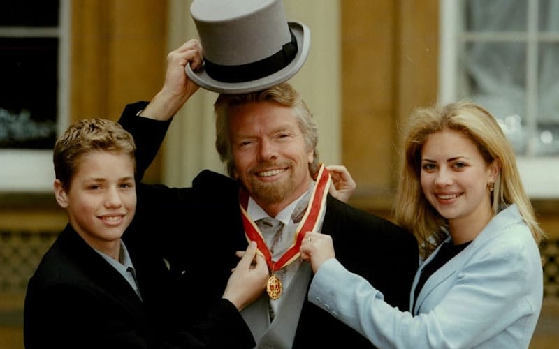 Richard Branson stands between his son and daughter who are smiling and holding his medal