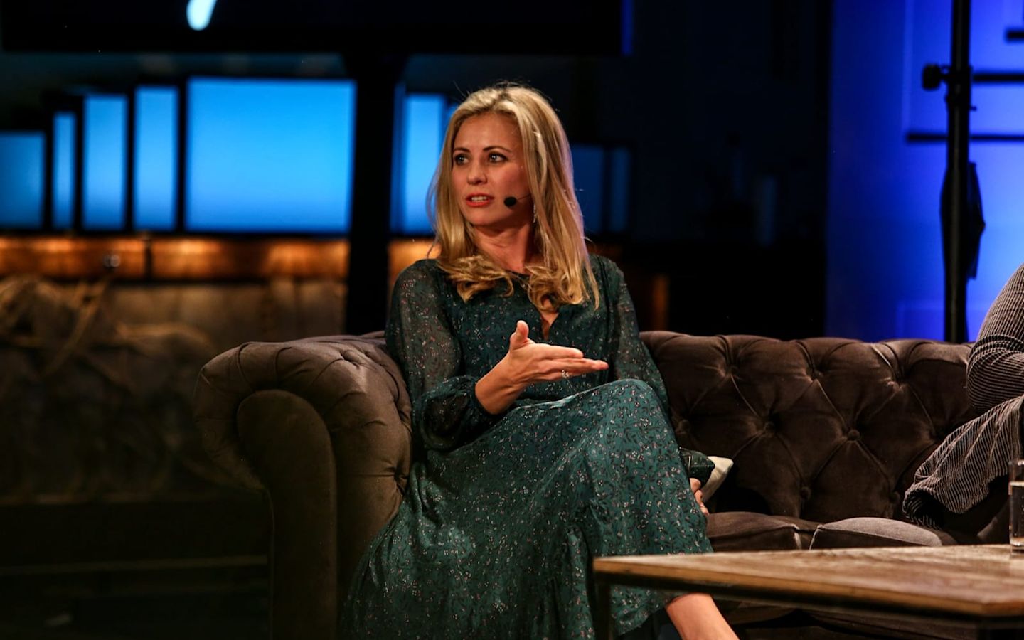 Holly Branson wearing a microphone, sitting on a brown sofa, looking away from the camera