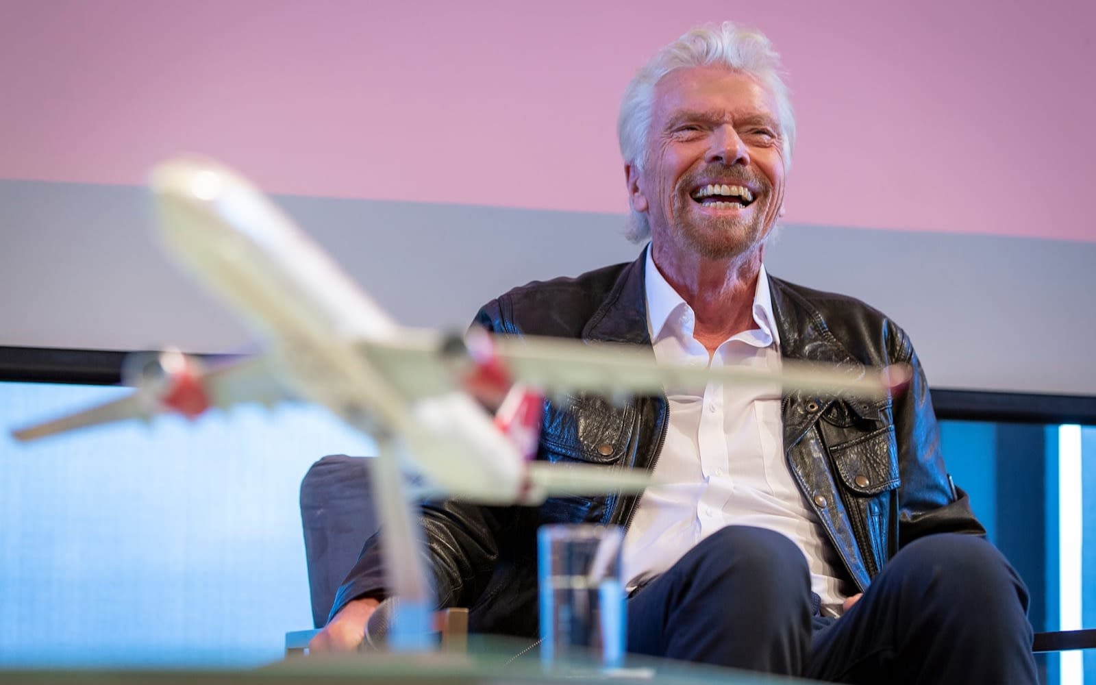 Richard Branson smiling with a model aeroplane in the foreground