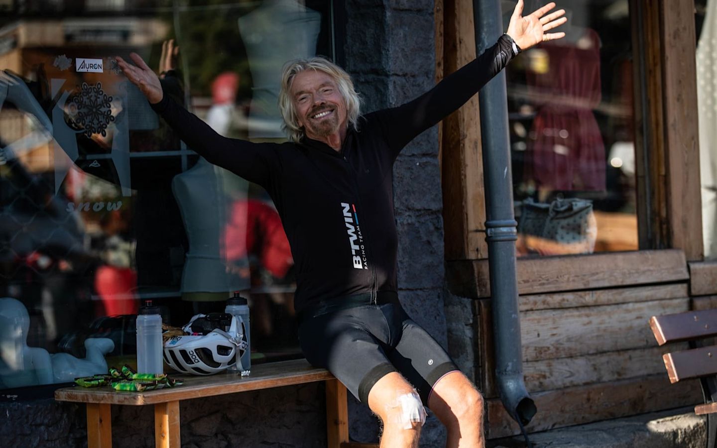 Richard with arms outstretched, sitting down smiling to camera in cycling gear