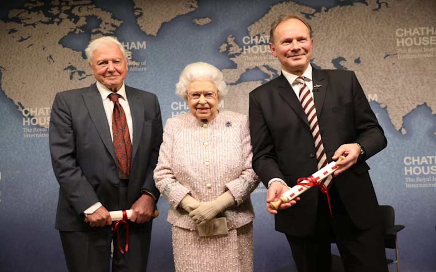 David Attenborough, the Queen and another gentleman stood in front of a large map