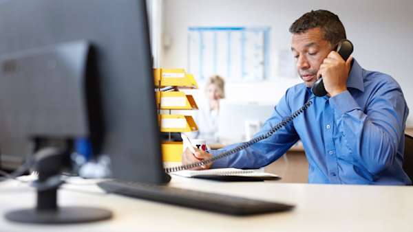 An office worker on a telephone whilst taking notes.