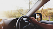 Driver's view inside a car, showing a hand on the steering wheel