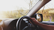 Driver's view inside a car, showing a hand on the steering wheel