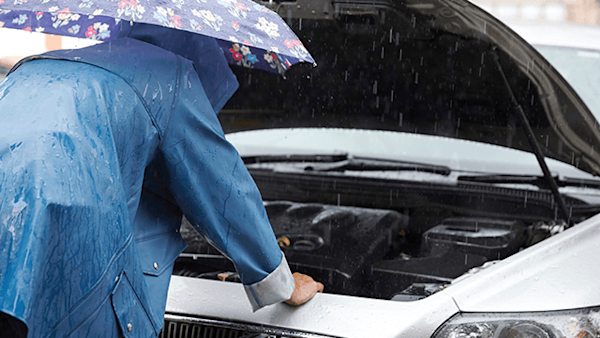 Driver looking under the car bonnet in the rain