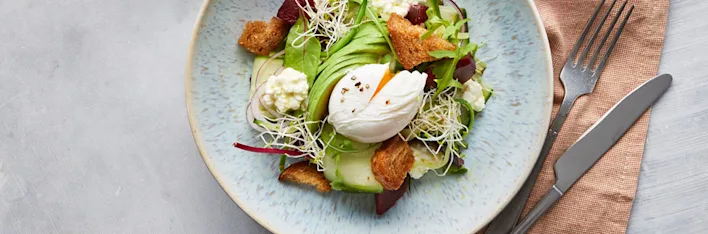 Vegetarisch recept van salade met avocado, gepocheerd ei, croutons en kiemgroenten.