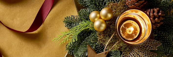 Sfeervolle kerstdecoratie met kaars, dennenappels en gouden accenten.