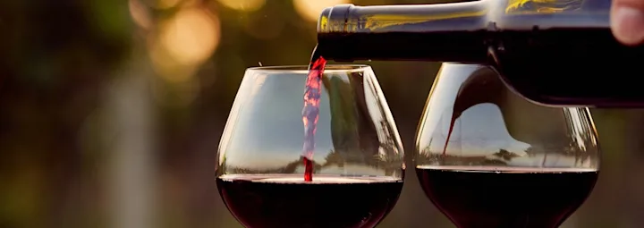 Rode wijn van PLUS wordt ingeschonken in een glas, met een tweede glas ernaast.