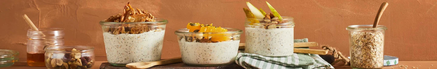 Overnight oats recepten: vier glazen potten met overnight oats, elk afgetopt met verschillende ingrediënten zoals granola, gedroogd fruit, sinaasappel en peer.