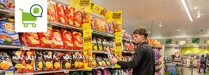 Klant bekijkt chips in supermarktgang met promotieborden voor smaakwedstrijd.