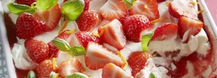 Aardbeiendessert met een laagje room, gegarneerd met verse aardbeien, basilicumblaadjes en geraspte citrusschil.