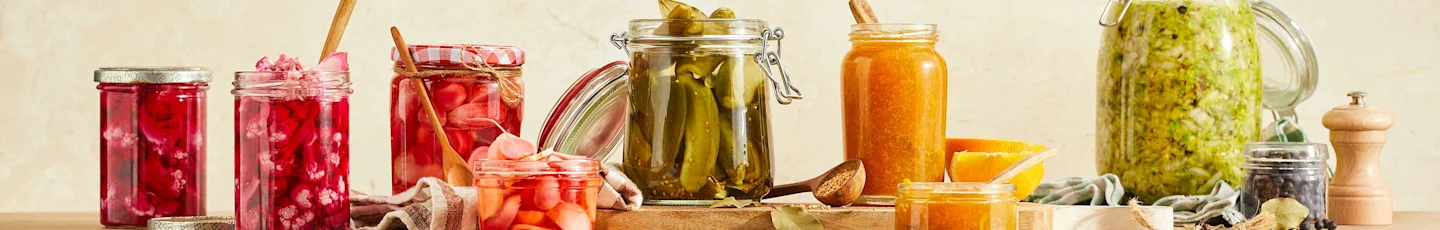Glazen potten met ingemaakte groenten, waaronder rode kool, wortels, komkommers en marmelade.