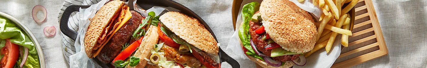 Drie BBQ-burgers met diverse toppings, geserveerd met friet en salade.