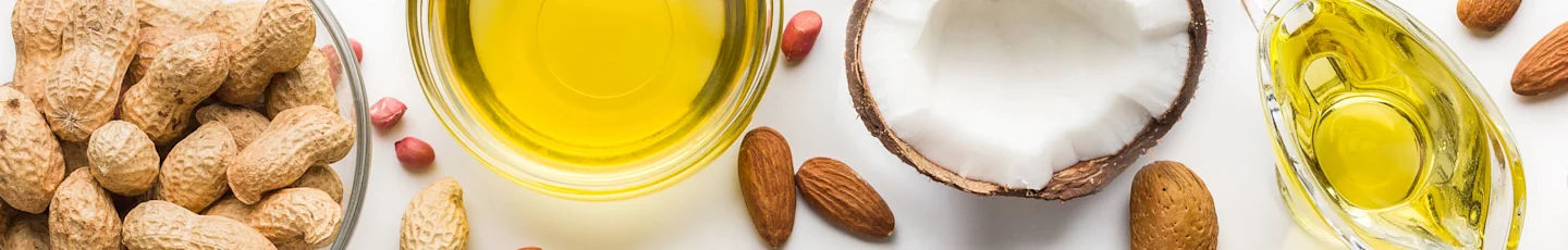Assortiment van noten en oliën: pinda’s in dop, amandelen, een gehalveerde kokosnoot en schaaltjes met olie.