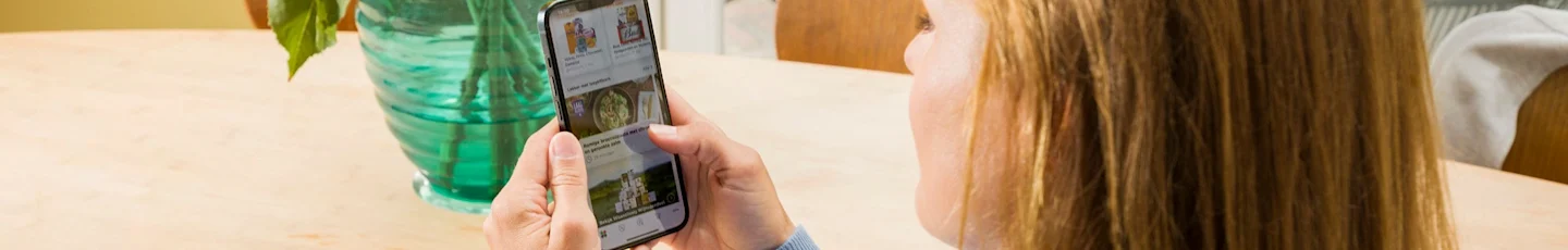 Persoon gebruikt smartphone aan tafel om boodschappen te bestellen bij PLUS.