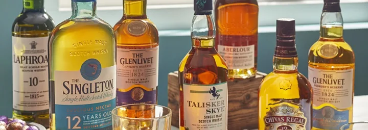 Selectie van whiskyflessen op tafel, met bekende merken als Laphroaig, The Singleton, The Glenlivet, Talisker Skye, Aberlour en Chivas Rega.