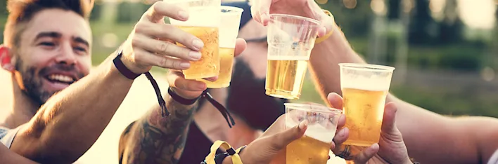 Groep mensen proost met plastic bekers bier tijdens een buitenevenement.