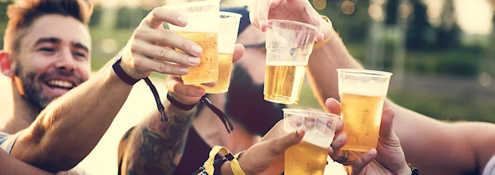 Groep mensen proost met plastic bekers bier tijdens een buitenevenement.