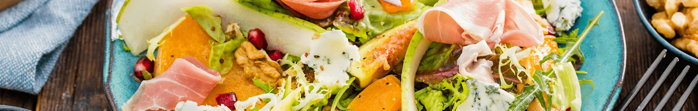 Wintersalade recept met plakjes peer, prosciutto, walnoten, granaatappelpitjes, gemengde sla en stukjes kaas.